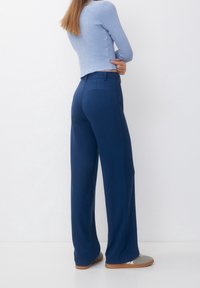 Pantalon large bleu marine à coupe structurée, avec poches avant et poche arrière. Associé à un haut côtelé bleu clair à manches longues et des chaussures décontractées.