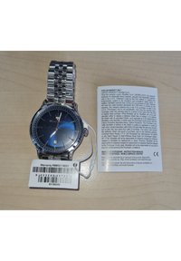 Sølv rustfrit stål armbåndsur med en blå gradient urskive, sølv timeindikatorer, dato vindue og et vedhæng, sammen med et garantikort.