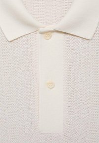 Hvid strikket polo shirt med et tekstureret design, der har en klassisk krave og to knaplukninger, lavet af blødt stof.