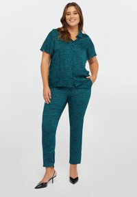 Completo due pezzi composto da una camicia a maniche corte e pantaloni aderenti in tessuto verde mare con un piccolo motivo a foglia nera. Scarpe nere con tacco.