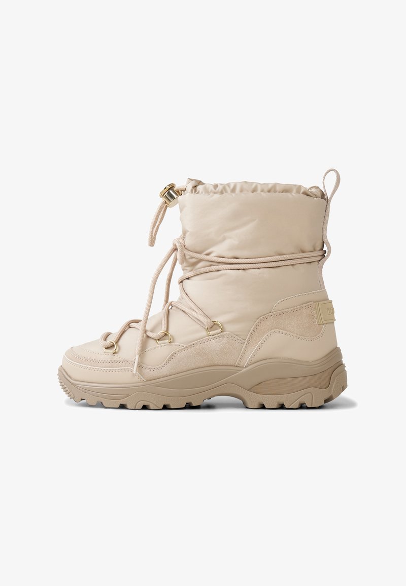 Beżowy wodoodporny but z miękką, wyściełaną cholewką, systemem sznurowania, gumową podeszwą i złotymi akcentami metalowymi. Charakteryzuje się teksturowaną cholewką i solidnym kształtem.