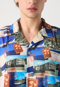 Kortærmet skjorte i blå stof med fotoprint, postkort og frimærker. Knaplukning og et afslappet kravedesign.