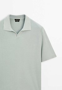 Polo gris clair à manches courtes avec une texture tricotée et un col doux, posé à plat sur un fond blanc.