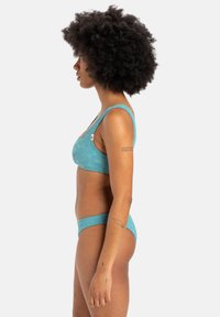 Zöldeskék bikini szett, texturált anyagból, virágmintákkal. A melltartó széles pántokkal rendelkezik, míg az alsó rész alacsonyan szabott.