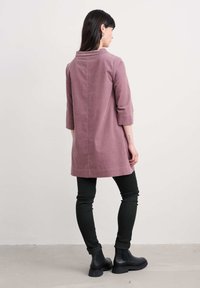 Tunic rosa, con texture, maniche a tre quarti, taglio dritto e fessure laterali, abbinata a jeans skinny neri e stivaletti.