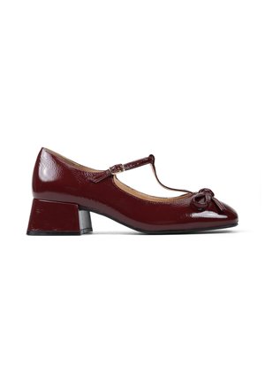 Buty w stylu Mary Jane z burgundowej lakierowanej skóry. Posiadają zaokrąglony czubek, mały akcent w postaci kokardki oraz słupkowy obcas. Pasek T z regulowanym zapięciem.
