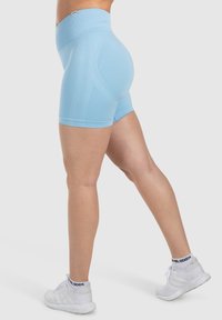 Shorts compressivi a vita alta di colore azzurro chiaro con una texture liscia, dotati di cuciture laterali e un design aderente, abbinati a scarpe da ginnastica bianche.
