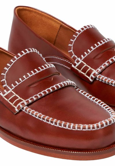 Mocasines de cuero marrón con costuras blancas, que cuentan con una ranura para moneda en el empeine y un acabado liso y pulido. La suela es plana y redondeada.