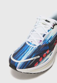Scarpa da corsa Nike con tomaia astratta multicolore in blu, nero e rosso. Materiale in rete e lacci bianchi, con il logo swoosh nero.