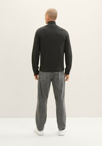 Dunkelgrauer gerippter Rollkragenpullover mit figurbetontem Schnitt, kombiniert mit lockeren grauen Jeans und weißen Sneakers, von hinten betrachtet.