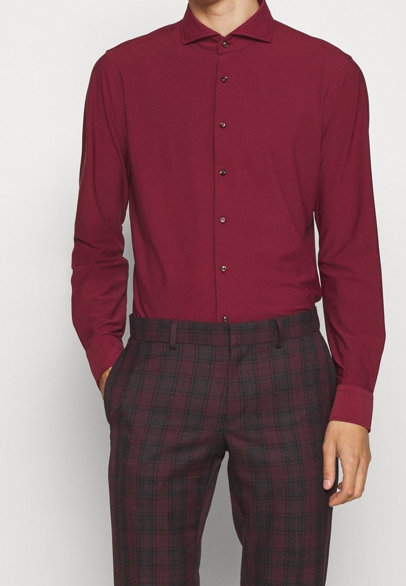 Camisa de manga larga burdeos con cuello puntiagudo, con botones negros y una textura suave, combinada con pantalones a rayas de un burdeos oscuro.