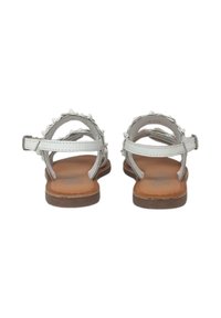 Sandali bianchi con punte decorative, suola piatta e cinturini alla caviglia. L'interno presenta un plantare in pelle marrone testurizzata per il comfort.