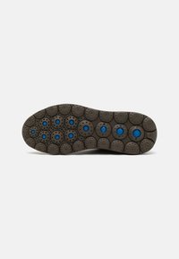 Suela de un zapato en caucho gris oscuro con un patrón de dibujo circular y acentos azules en el centro de cada círculo. Diseño redondeado y texturizado.