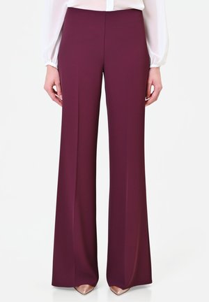 Donna che indossa pantaloni bordeaux a vita alta e gamba larga abbinati a una camicetta bianca a maniche lunghe e scarpe beige a punta.