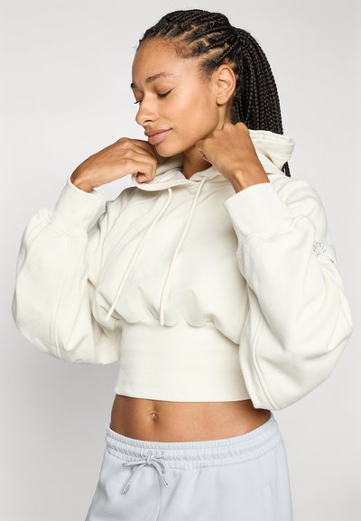 Korte crèmekleurige hoodie van zachte stof met volumineuze mouwen en trekkoorden, gecombineerd met lichtgrijze sweatpants.