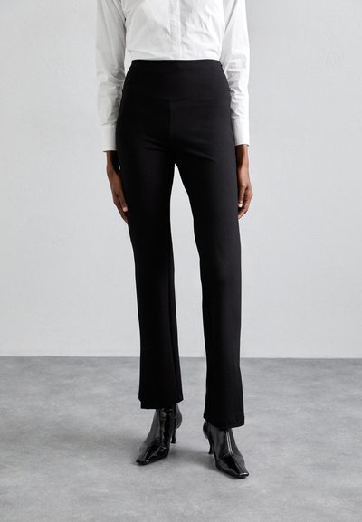 Schwarze, ausgestellte Hosen mit hoher Taille, aus glattem Material gefertigt. Sie verfügen über ein elegantes Design und passen gut zu spitzen schwarzen Stiefeln.