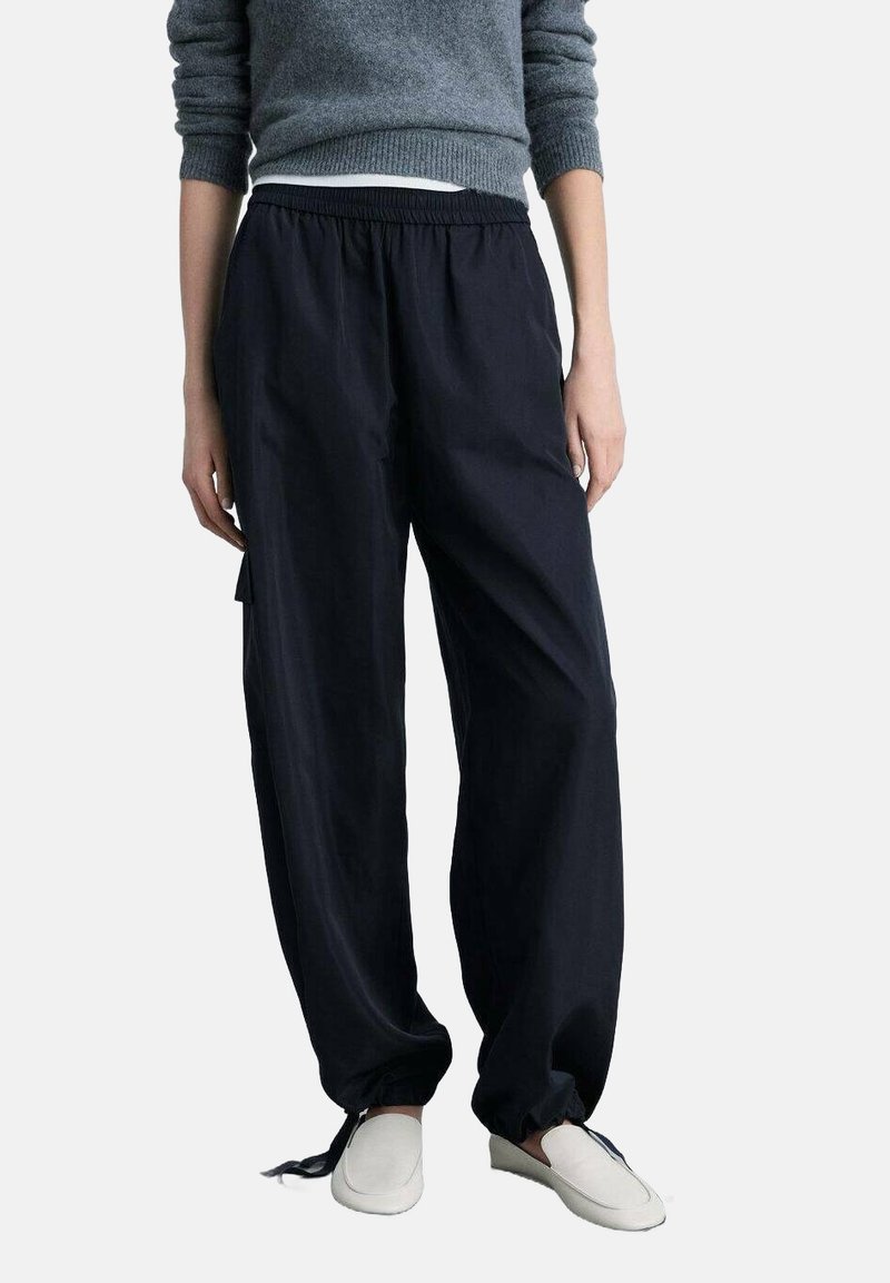 Marineblauwe broek met elastische tailleband, ontspannen pasvorm en zijzakken, gemaakt van lichtgewicht stof. Gedragen met platte, lichtgekleurde schoenen.