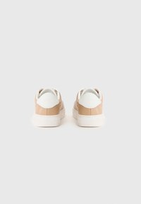 Baskets en cuir tan avec des accents blancs, présentant une texture lisse, un bout rond et une semelle en caoutchouc plate. Design minimaliste avec des détails de couture.
