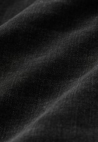 Gros plan de la texture d'un tissu noir montrant un tissage fin et des plis doux sous un éclairage doux.
