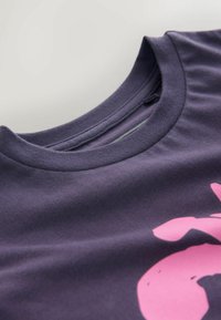 Purple cotton t-shirt with a crew neckline, featuring a prominent pink graphic design. Soft texture, visible stitching details along the collar.