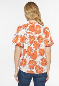 Blumenbluse in Weiß mit großen orangen Blumen und schwarzen Umrandungen, mit kurzen Puffärmeln und Paspelierungen auf der Rückseite.