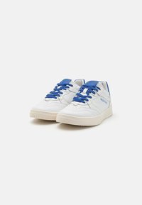 White leather sneakers featuring blue accents, textured surface, perforated toe, and flat laces. Thick rubber sole with a slight tread pattern.