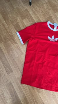 Κόκκινη βαμβακερή μπλούζα T-shirt με άσπρες λεπτομέρειες στον γιακά και τα μανίκια, και με ένα χαρακτηριστικό άσπρο λογότυπο trefoil στο μπροστινό μέρος.