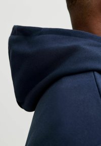 Marineblauwe hoodie met een zachte, gestructureerde stof, met een close-up van de gevormde capuchon en kraag.