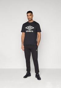 Sort bomulds t-shirt med hvid "umbro" logo, parret med sorte sweatpants og sorte sportssko. Enkel, afslappet design.