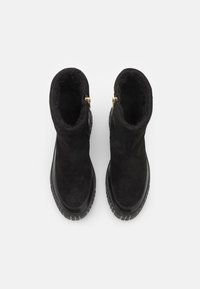 Botas negras de tobillo con parte superior de ante, forro suave y suela de goma. Presentan herrajes en tono dorado y un diseño sin costuras con punta redondeada.