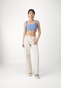 Top court côtelé bleu clair avec encolure carrée, associé à un pantalon large crème ; modèle portant des talons beiges et des boucles d'oreilles circulaires.
