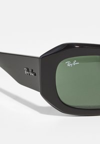 Ochelari de soare supradimensionați, negri, cu lentile verzi. Caracteristicile includ un design al ramei geometric și logo-ul Ray-Ban pe lateral.