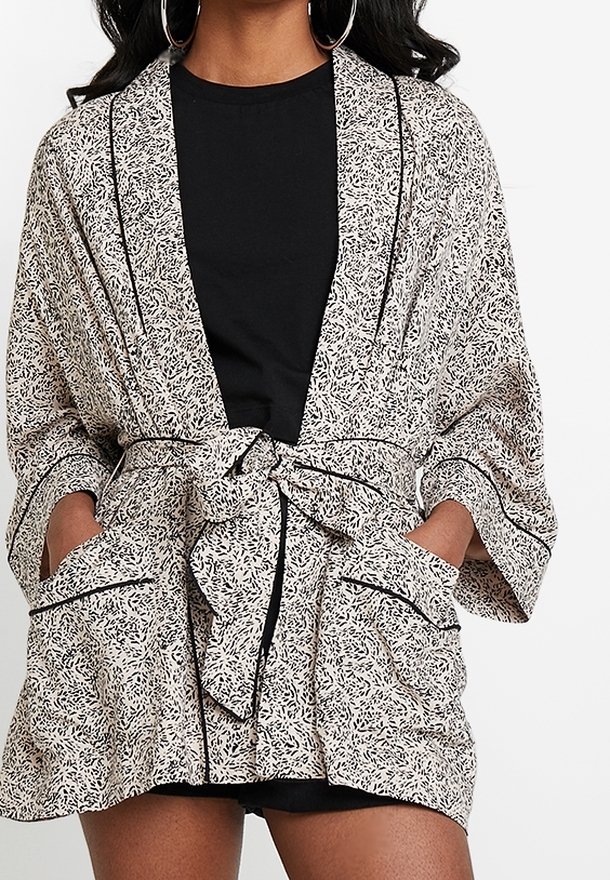Kimono con estampado floral en blanco y negro, con un lazo en la cintura, mangas anchas y dos bolsillos frontales con detalles en pipa negra.