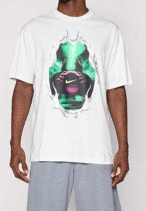 Mann trägt weißes T-Shirt mit farbenfroher Grafik einer Figur, die einen Basketball hält, mit einem leuchtenden Nike-Logo in grünen und violetten Tönen.