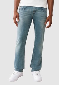 Jasnoniebieskie dżinsy, prosty krój nogawki, średni stan, subtelne przetarcia, klasyczny pięciokieszeniowy design, w połączeniu z białymi trampkami.