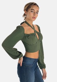 Grøn kortærmet bluse med puffede ærmer og en nøglehulåbning, lavet af blødt stof. Sammen med tætsiddende blå jeans.