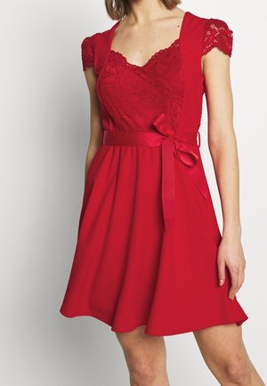 Robe rouge avec un corsage en dentelle, manches courtes et taille cintrée. Jupe évasée avec poches et un détail de ceinture en ruban assorti.