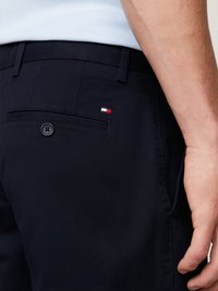Marineblå shorts med en glatt tekstur, med en baklomme og en liten rød, hvit og blå logo-detalj. Synlig knappelukking.