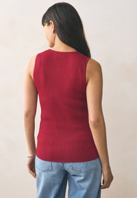 Red ribbed knit sleeveless top with a fitted design, highlighting vertical stripes and a rounded neckline at the back.