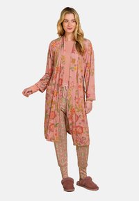 Lange roze badjas met bloemmotieven, gecombineerd met gestreepte groene leggings en comfortabele bruine slippers. Zacht materiaal met een ontspannen pasvorm.