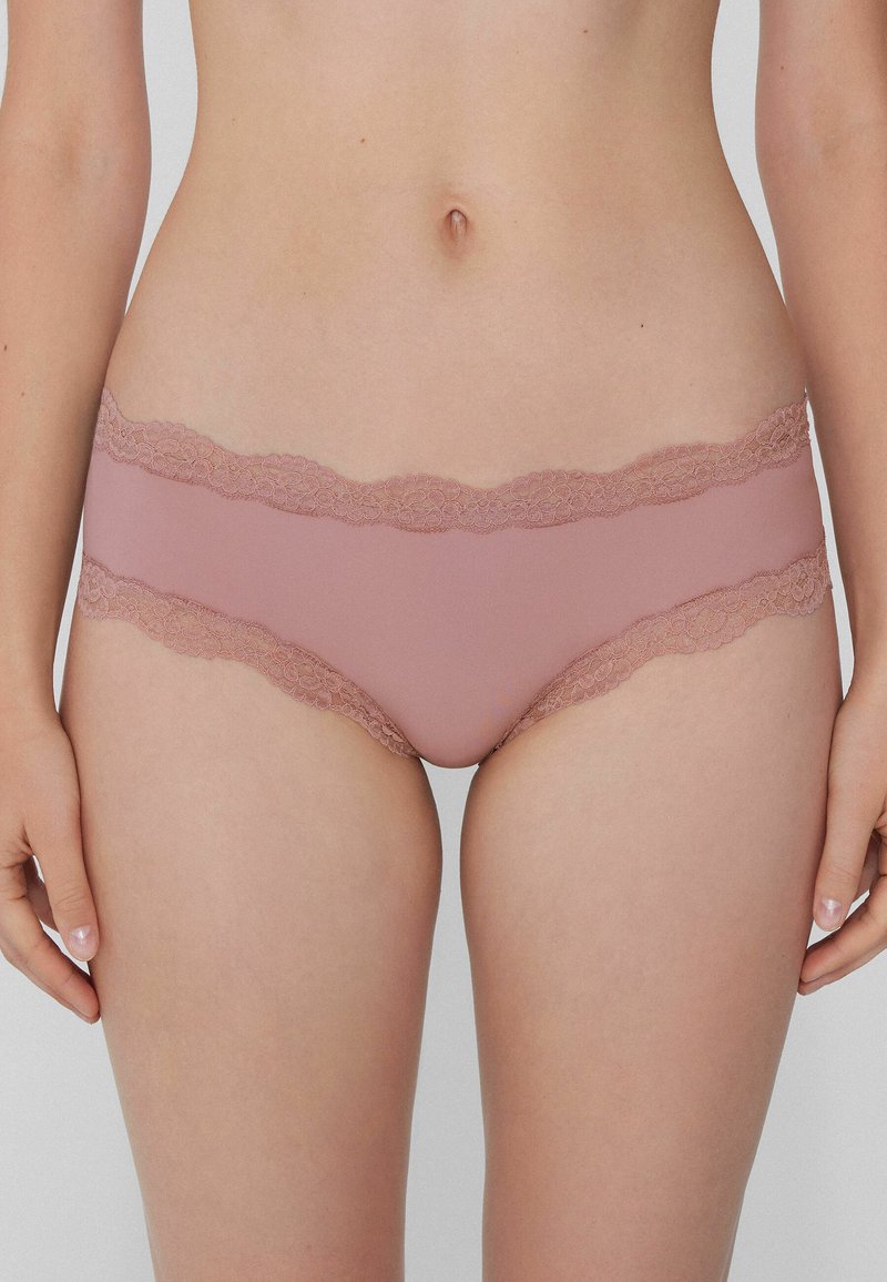 Světlé růžové spodní prádlo s krajkovým lemem, vyrobené z hladké látky, s vlnitými okraji a nízkým pasem, navržené pro pohodlí a skvělé padnutí.