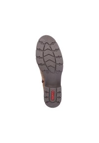 Des chaussures brunes avec une semelle en caoutchouc texturé. La semelle présente un motif de crampons pour une meilleure adhérence et le nom de la marque "rieker" en rouge.