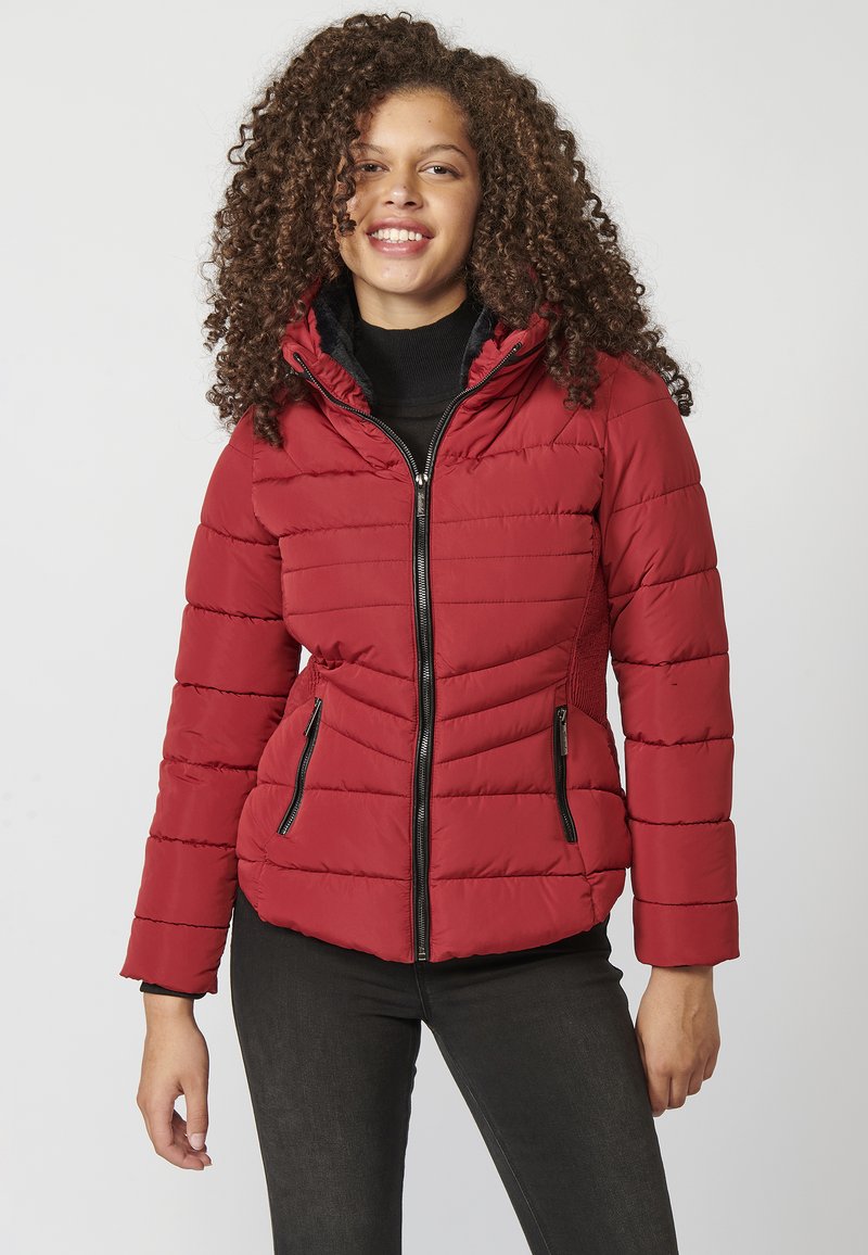 Sarkans pufīgs jakas ar kvadrātveida šuvēm, ar rāvējslēdzēju priekšā un kapuci. Iezīmētas ar melnām rāvējslēdzēju kabatām un pieguļošu siluetu.