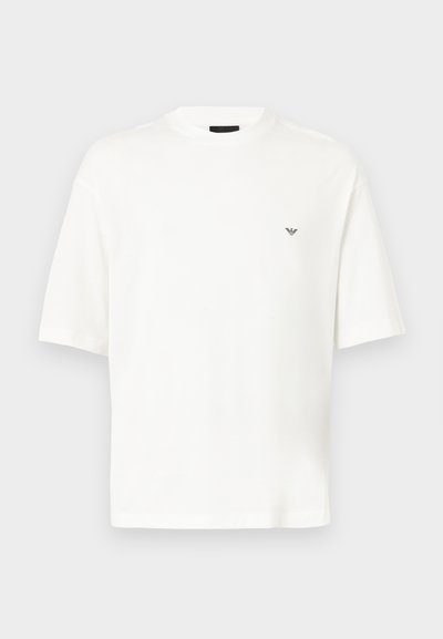 Άσπρο κοντομάνικο t-shirt με στρογγυλή λαιμόκοψη και μικρό μαύρο λογότυπο στο αριστερό στήθος, απεικονισμένο σε απλό ανοιχτό γκρι φόντο.