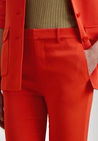 Felle rode op maat gemaakte colbert met bijpassende slim-fit broek. Het materiaal lijkt glad, met een klassieke snit en zijzakken.