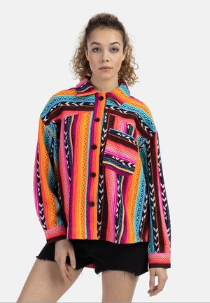 Kleurrijk oversized shirt met levendige strepen en patronen in oranje, roze, blauw en zwart; met knoopsluiting aan de voorkant en een borstzak.