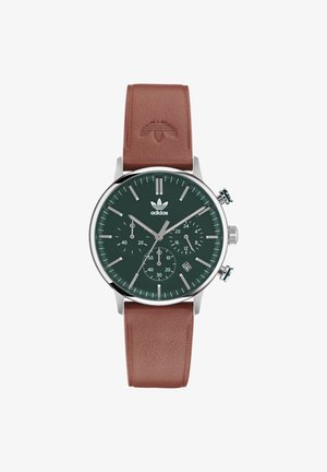 Zaļš pulksteņa ciparnīca ar sudraba elementiem, brūna ādas siksna, hronogrāfa funkcijas un datuma rādītājs netālu no pulksteņa 4.