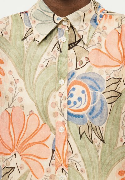Chemise à col avec fermeture à boutons, présentant un imprimé floral dans des tons pastel d'orange, de bleu, de vert et de beige sur un tissu texturé.