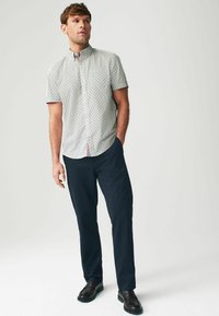 Camisa de manga corta con un patrón geométrico azul claro, diseño con cuello y acentos rojos en la placket de botones, combinada con pantalones oscuros.