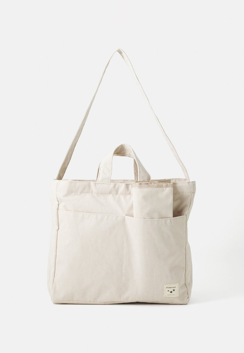 Beige ribbed fabric tote bag with dual handles and an adjustable shoulder strap, featuring an exterior pocket and a small logo label.